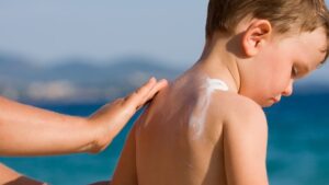 Kid having sunburn applied to his back at the beach by his parent